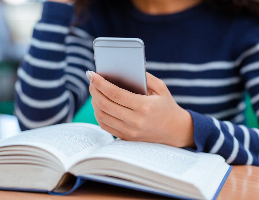 female hand holding a cell phone while reading book